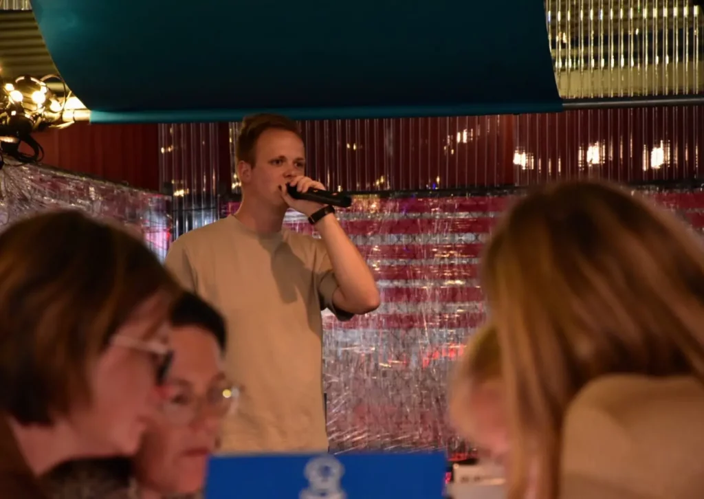 Gezellige pubquiz sfeer met mensen die lachen en een quizmaster op de achtergrond.